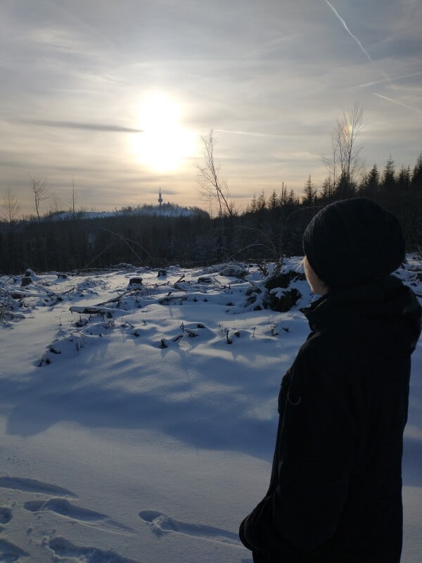 Person, die in die verschneite Winterlandschaft des Ravensbergs zur untergehenden Sonne schaut