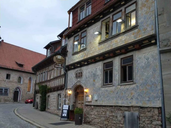 Mühlhausen Antoniusmühle - Außenansicht, urige Eingangstür mit Aufsteller, Blumenkübel und Laterne davor, ein altertümliches Schild an der Hauswand zeigt den Namen