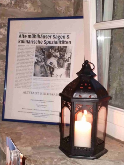 Mühlhausen Antoniusmühle - schwarze Laterne mit brennender Kerze im Fensterrahmen, daneben ein Bilderrahmen mit der Sage der Antoniusmühle