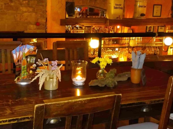 Mühlhausen Antoniusmühle - Tisch mit Kerzen, Vasen, Kartenaufsteller und Gefäß mit Besteck, im Hintergrund Blick von Empore über Geländer auf Tresen im Gastraum