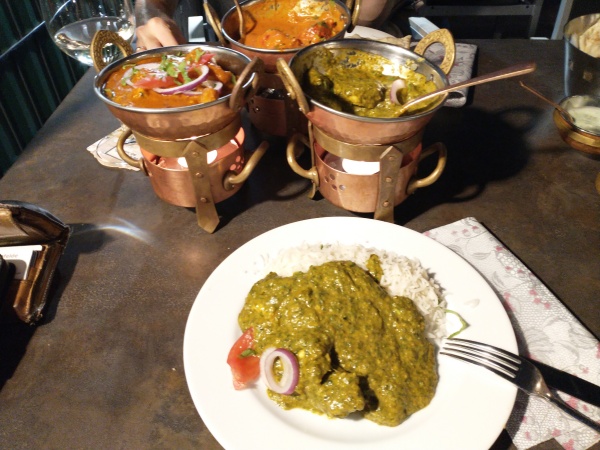 indisch essen gehen im Ganesha in Mühlhausen - auf einem Tisch steht ein Teller mit Reis und einer großen Portion Chicken Palak (Hähnchen in Spinat), im Hintergrund drei für indische Restaurants typische Servierschalen, zum Teil nur noch halb gefüllt mit verschiedenen Gerichten